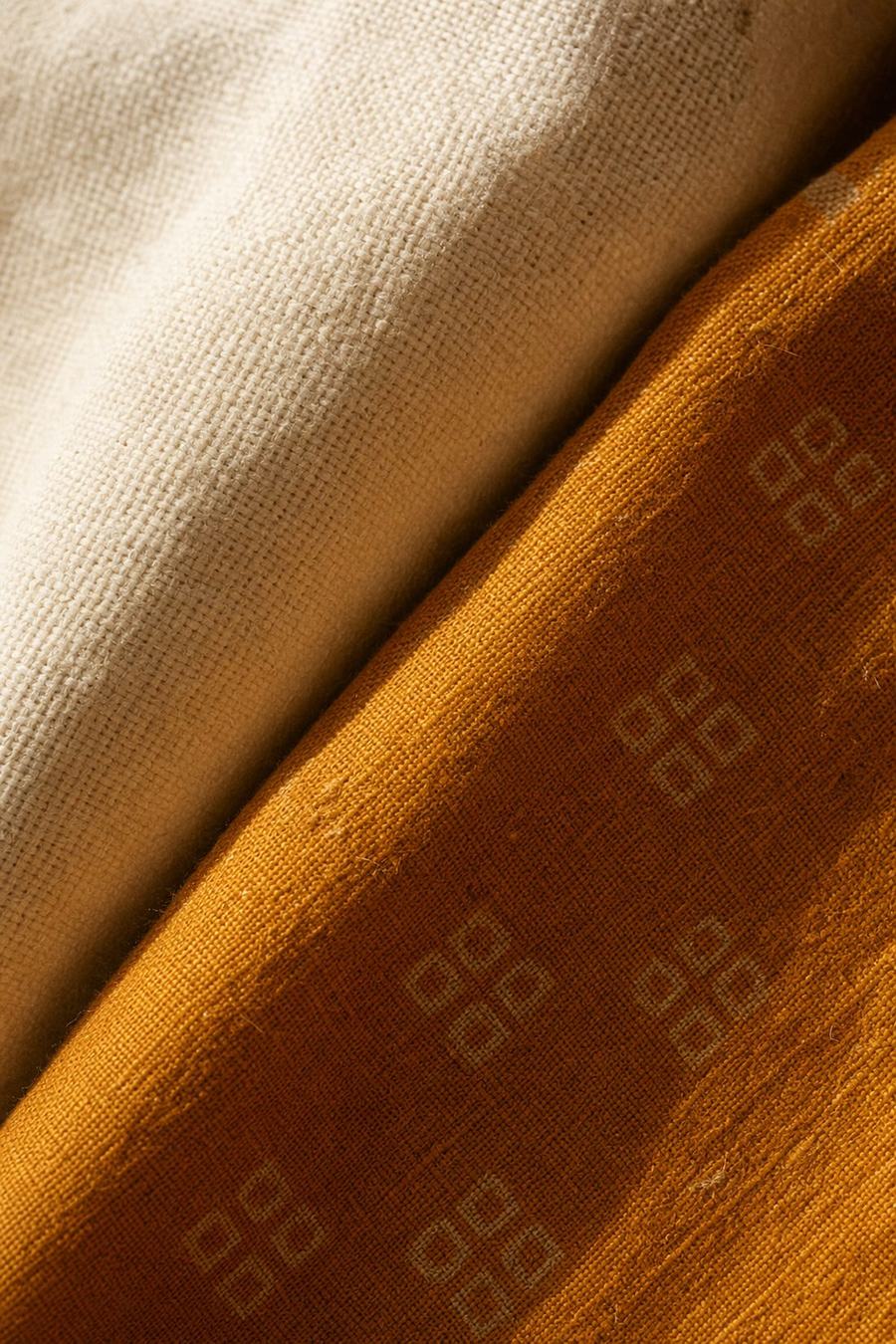 Close-up of undyed cream cloth overlapping deep saffron block-printed cloth in raking daylight.